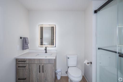 A white bathroom with a sink, mirror, toilet and a glass shower door.at The Jones Tower at the Collective, Pittsburgh, PA 15203