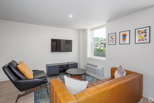 A living room with a black leather chair, a brown sofa, and a flat screen TV mounted on the wall.at The Jones Tower at the Collective, Pittsburgh, PA 15203