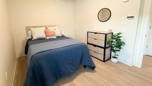 A bedroom with a bed, nightstand, and a plant.at The Jones Tower at the Collective, Pittsburgh, PA 15203