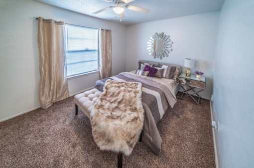 A bedroom with a bed, a bench, and a window with curtains.