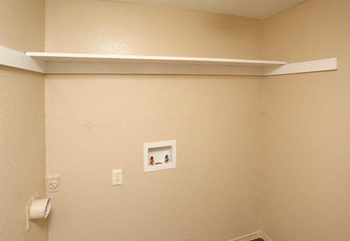 A white shelf is mounted on a tan wall above a toilet paper roll.