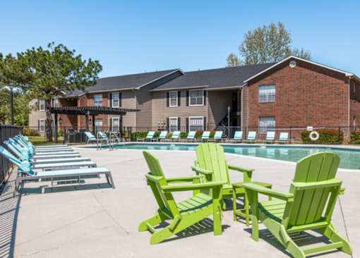 A row of green Adirondack chairs are lined up by a pool.