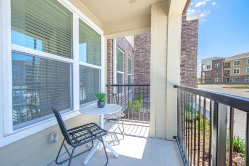 a balcony with a small table and two chairs and a brick building in the background at Alta Denton Station, Denton, Texas