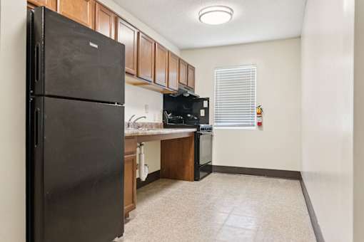 A black refrigerator is in a kitchen with wooden cabinets.