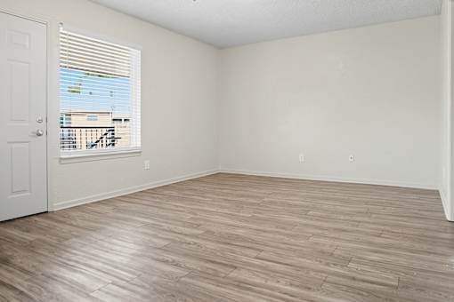 A room with wooden flooring and a view of a balcony through the window.