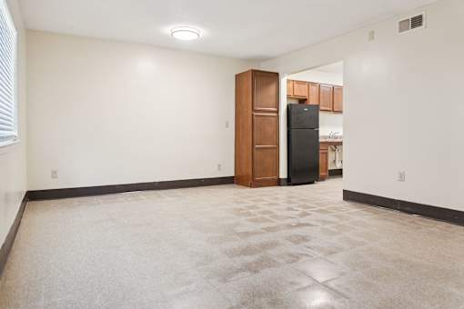 A spacious room with a carpeted floor and a black refrigerator in the corner.