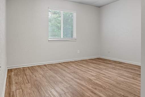 A room with wooden flooring and a window with blinds.