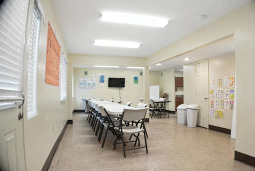 A classroom with white tables and chairs, a whiteboard, and posters on the walls.