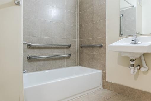 A white bathtub sits next to a sink in a tiled bathroom.