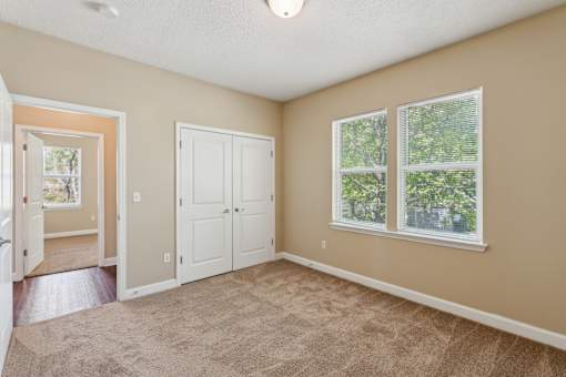 A room with a carpeted floor, a white door, and a window with a view of trees.
