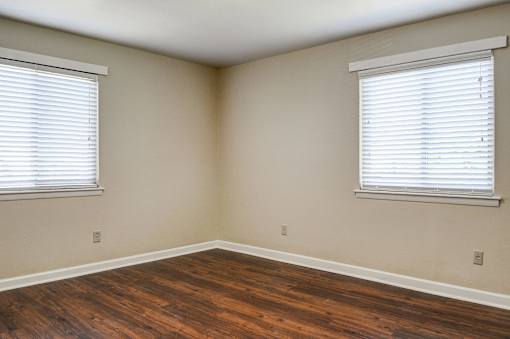 A room with wooden floors and two windows with blinds.