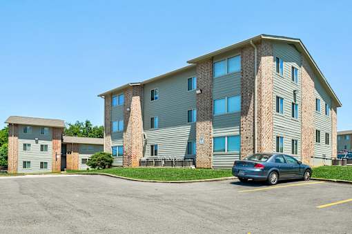 A blue car is parked in a parking lot in front of a large apartment building.