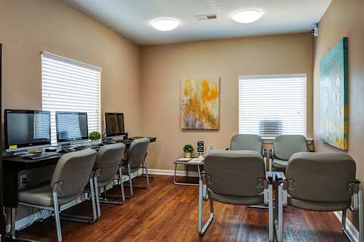 A room with a desk and chairs with a painting on the wall.