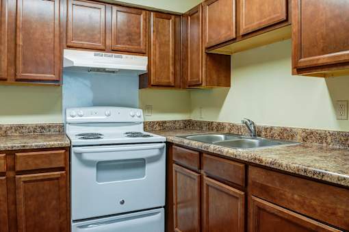 A white stove and sink in a kitchen with brown cabinets.