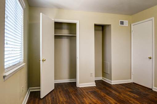 A room with a white door, a window with blinds, and a wooden floor.