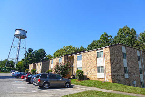 A parking lot with cars and a water tower in front of a brick apartment building.