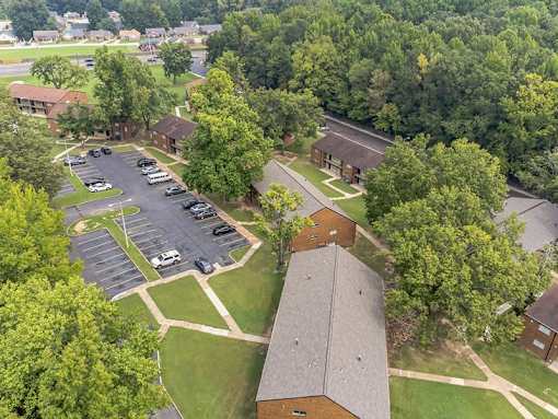 A parking lot is surrounded by trees and a building.