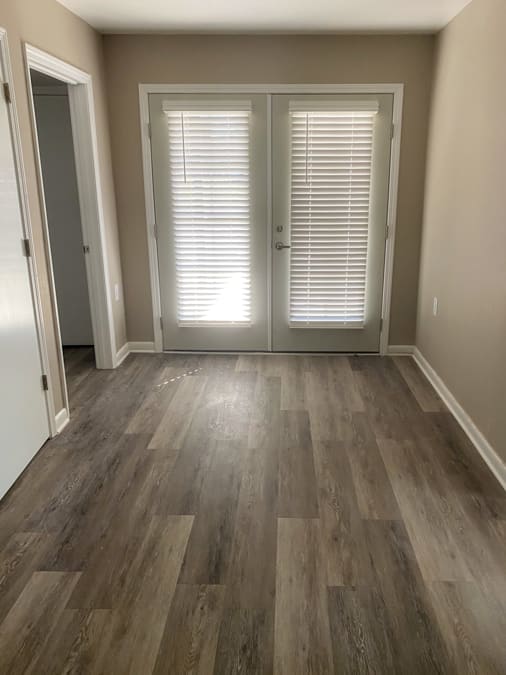 A room with a wooden floor and a white door with blinds.
