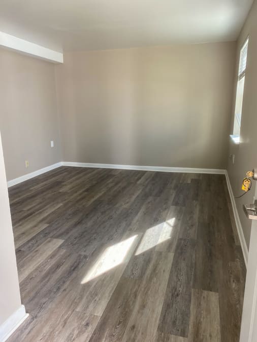 A room with wooden flooring and a window letting in sunlight.
