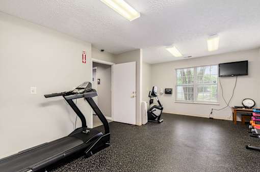 A room with a treadmill, vacuum, and television.