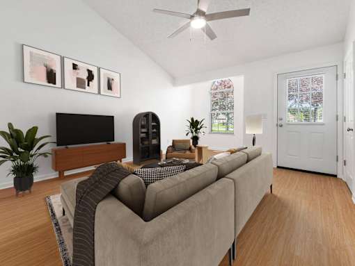A living room with a grey couch, a television, a plant, and a fan.