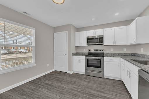 modern kitchen with window and white cabinets along with stainless steel appliances