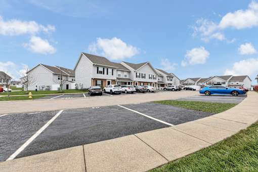 A parking lot in front of a row of houses with cars parked.