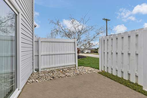 A white fence and a grey concrete pathway in front of a house.
