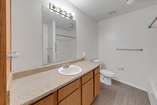 A bathroom with a sink, mirror, toilet and a shower.