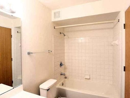 A white tiled bathroom with a toilet, sink, and bathtub.