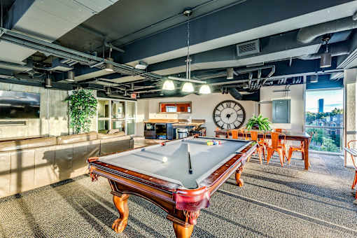 A pool table is in the middle of a room with a clock on the wall.