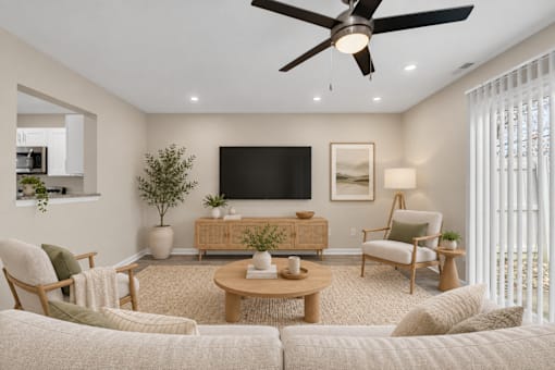 A living room with a white couch, a wooden coffee table, a flat screen TV, and a ceiling fan.