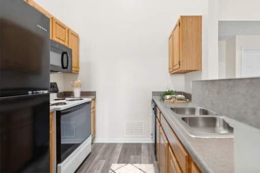 A kitchen with a black refrigerator and microwave, wooden cabinets, and a sink.
