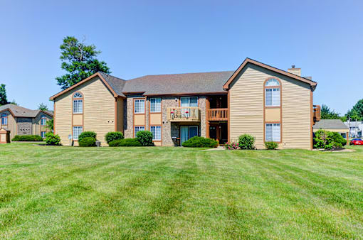 A large house with a brown roof and tan siding with a green lawn in front.