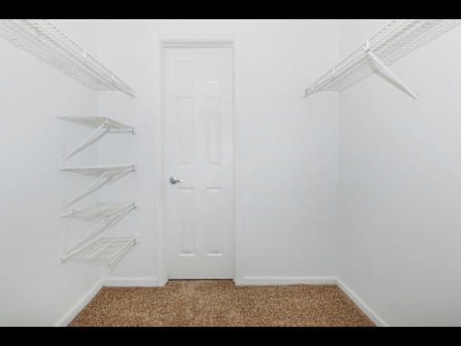 A white door is in the middle of a room with white walls and a brown carpet.