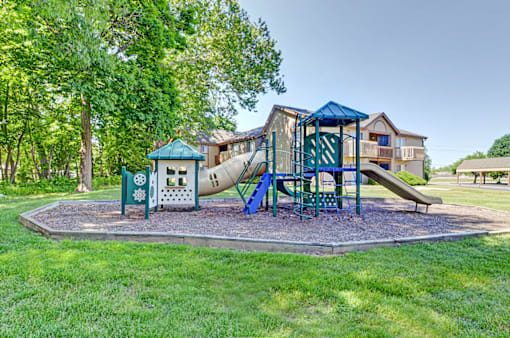 A playground with a green slide and a blue canopy is in the foreground of a residential area.