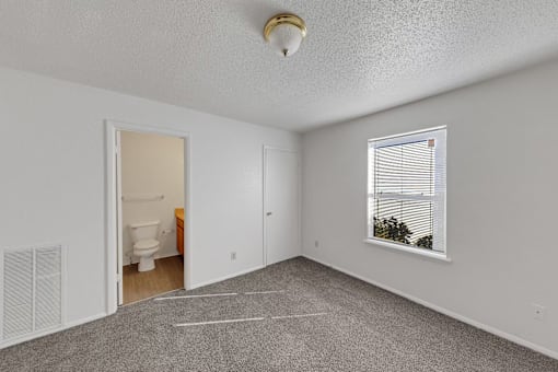 A room with a carpeted floor, a window with blinds, and a door leading to a bathroom.