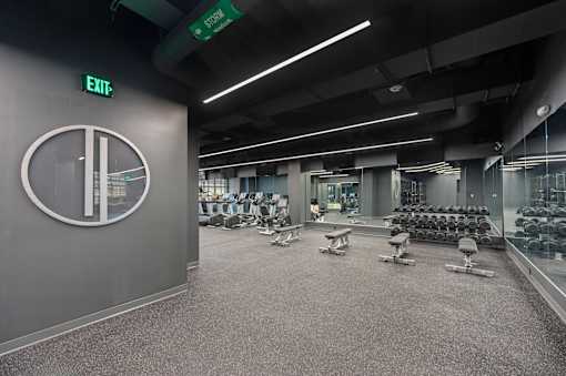 A gym with a green exit sign and a clock on the wall at Sky Central Apartments, Cincinnati