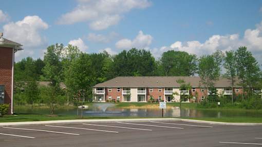 A parking lot in front of a building with a fountain in the middle.