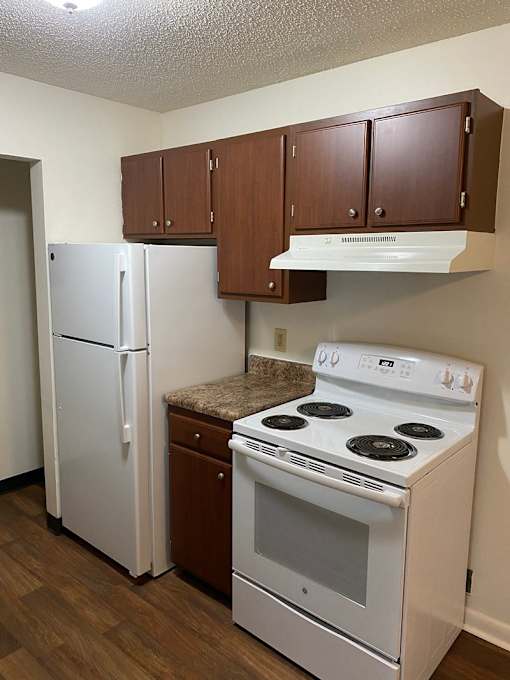 A white fridge and stove in a kitchen with brown cabinets.
