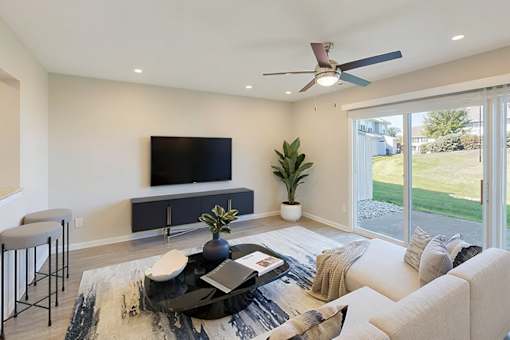 A modern living room with a flat screen TV, a coffee table, and a ceiling fan.