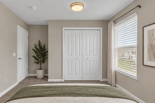 A bedroom with a bed, a plant, and a framed picture on the wall.