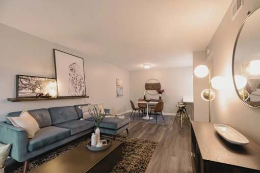 A modern living room with a grey sofa, a coffee table, and a round mirror on the wall at A62 Apartments, Indianapolis