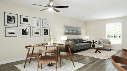 A living room with a grey couch, a wooden table and chairs, a rug, and a ceiling fan at A62 Apartments, Indianapolis