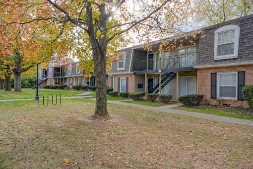 A tree with orange leaves stands in front of a brick building with a balcony at A62 Apartments, Indianapolis, IN