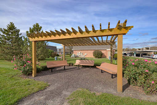 A wooden pergola with benches is situated in a grassy area at A62 Apartments, Indianapolis, IN