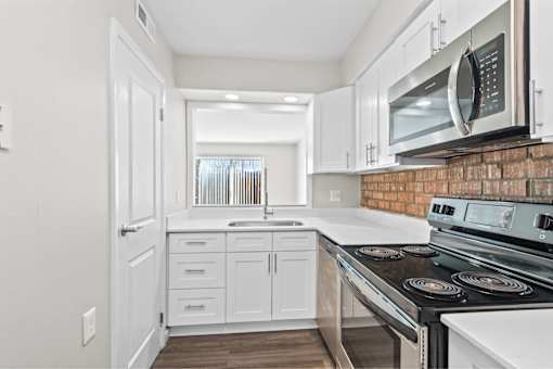 A kitchen with white cabinets and a brick backsplash.