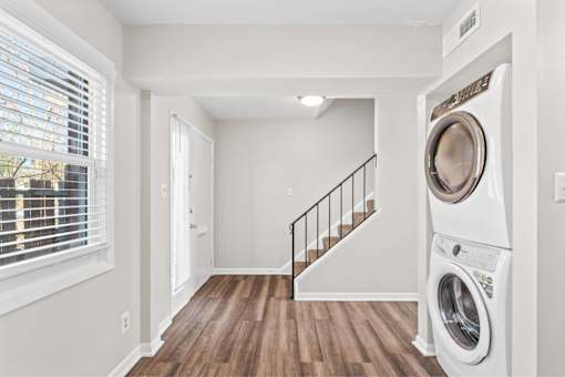 A white washing machine is in a laundry room with a staircase.