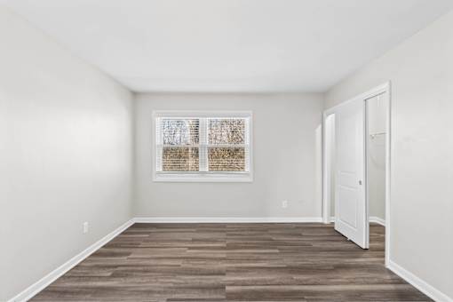A room with a wooden floor and a window with blinds.