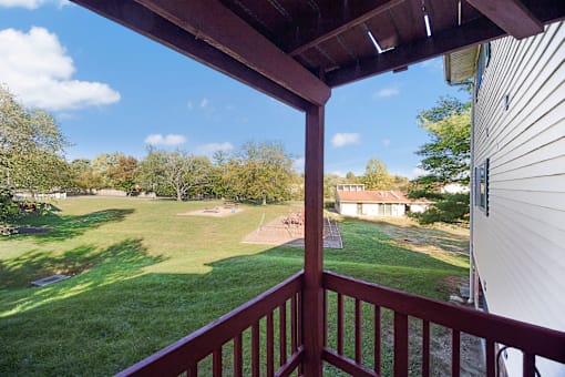 A view from a balcony overlooking a green lawn and a house.